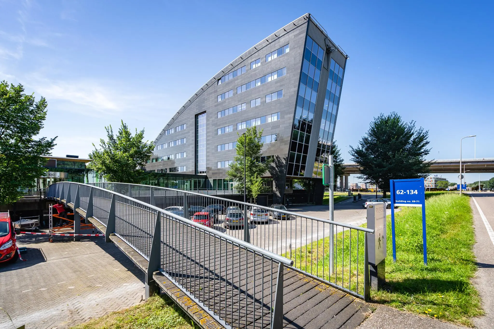 Modern kantoorgebouw aan de Rivium Promenade met opvallende architectuur en voetgangersbrug op de voorgrond.